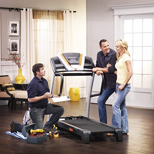 Three people setting up a treadmill in a bright living room.